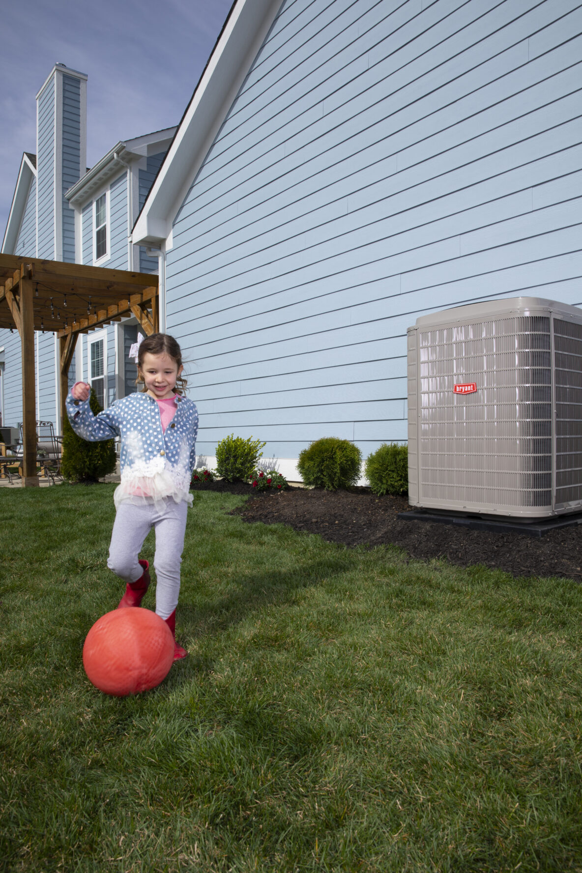 Little girl kicking red ball in yard by Bryant HVAC unit. Superior Heating Cooling Plumbing blog image.